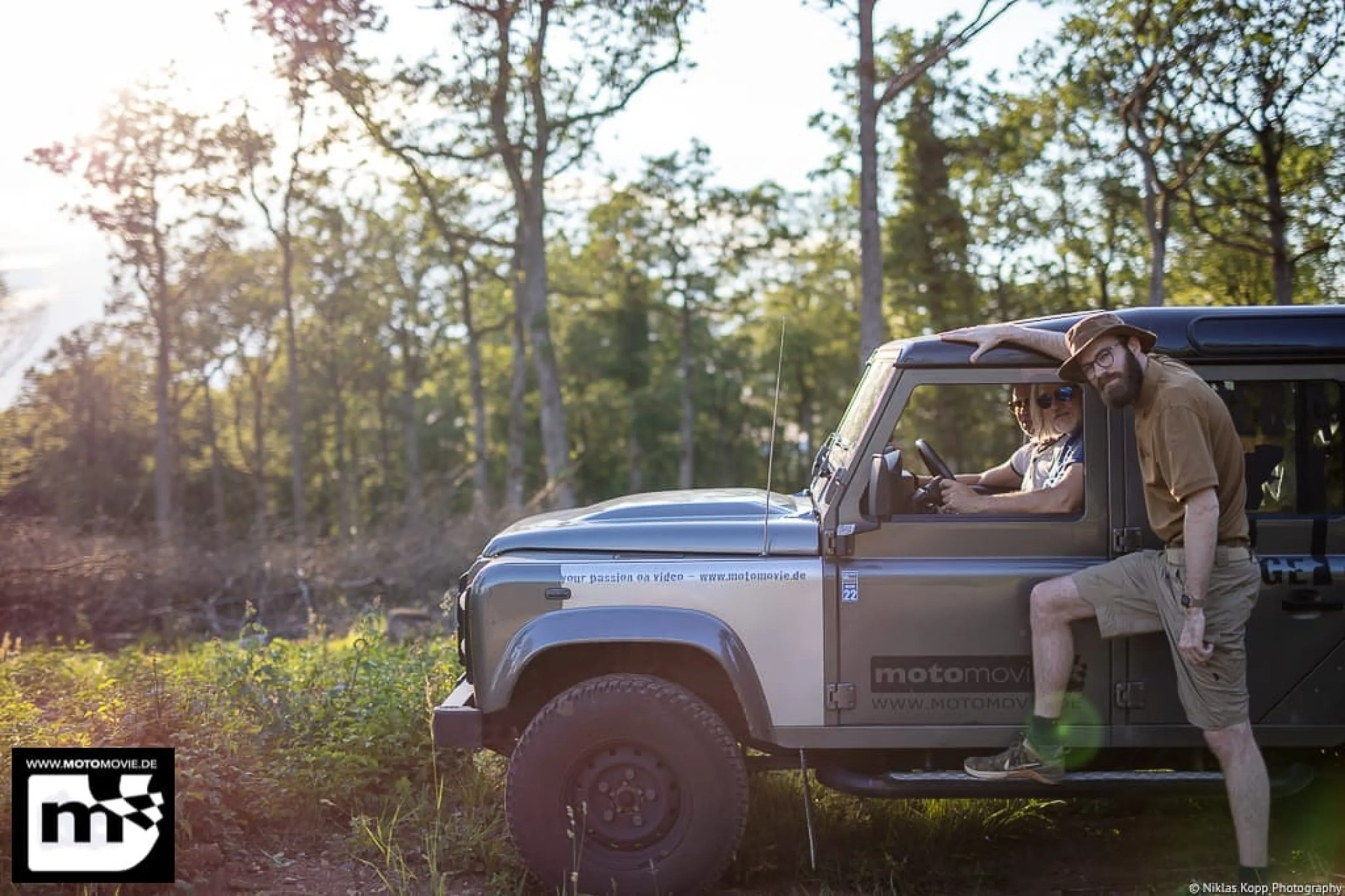 Two travellers beside an off-road vehicle in warm evening light