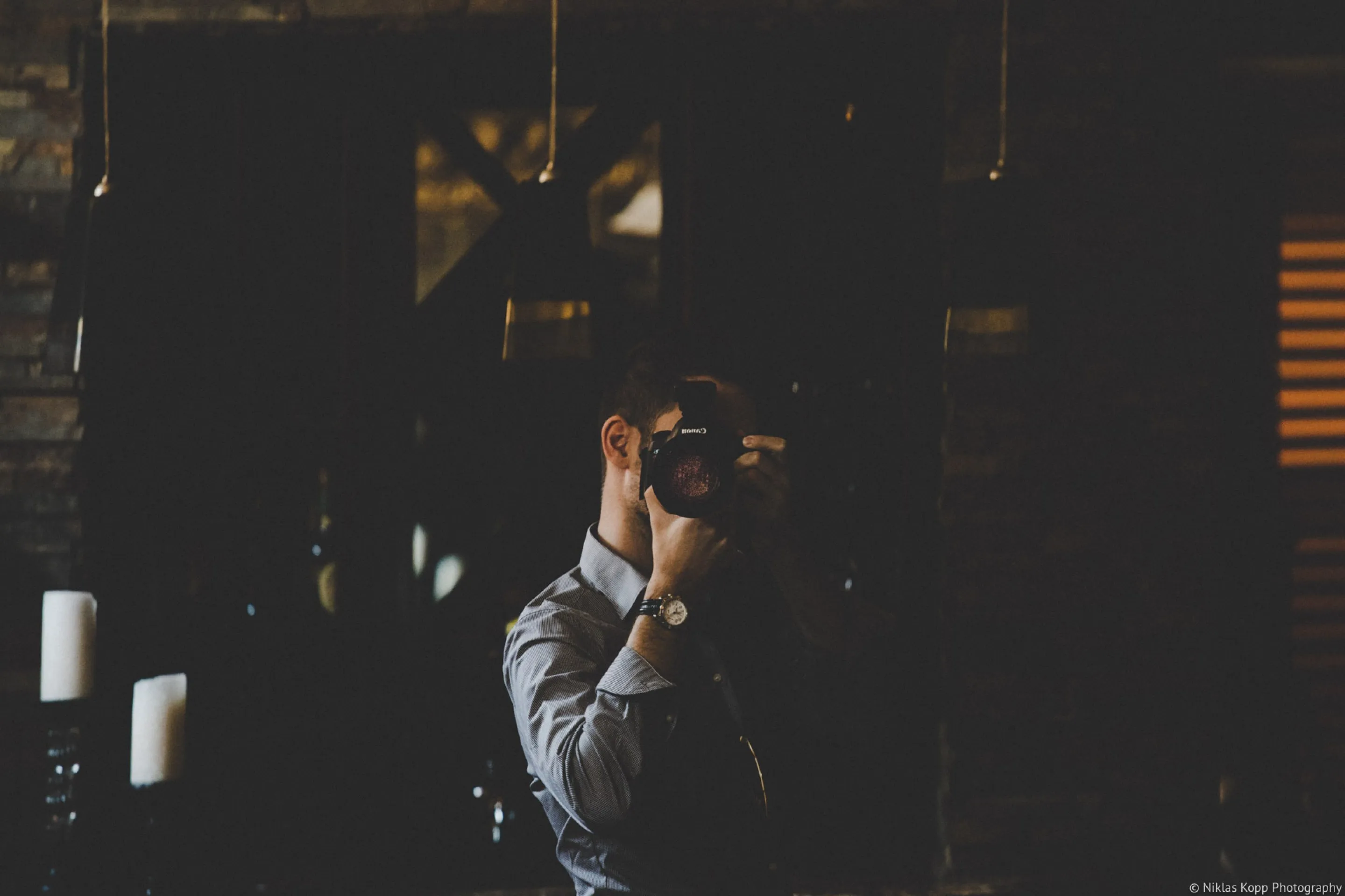 Dark mirror self-portrait of Niklas Kopp holding a camera in front of his face